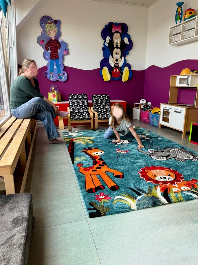 Spielbereich mit großer Fensterfront, kindgerechter Wandgestaltung und Spielteppich